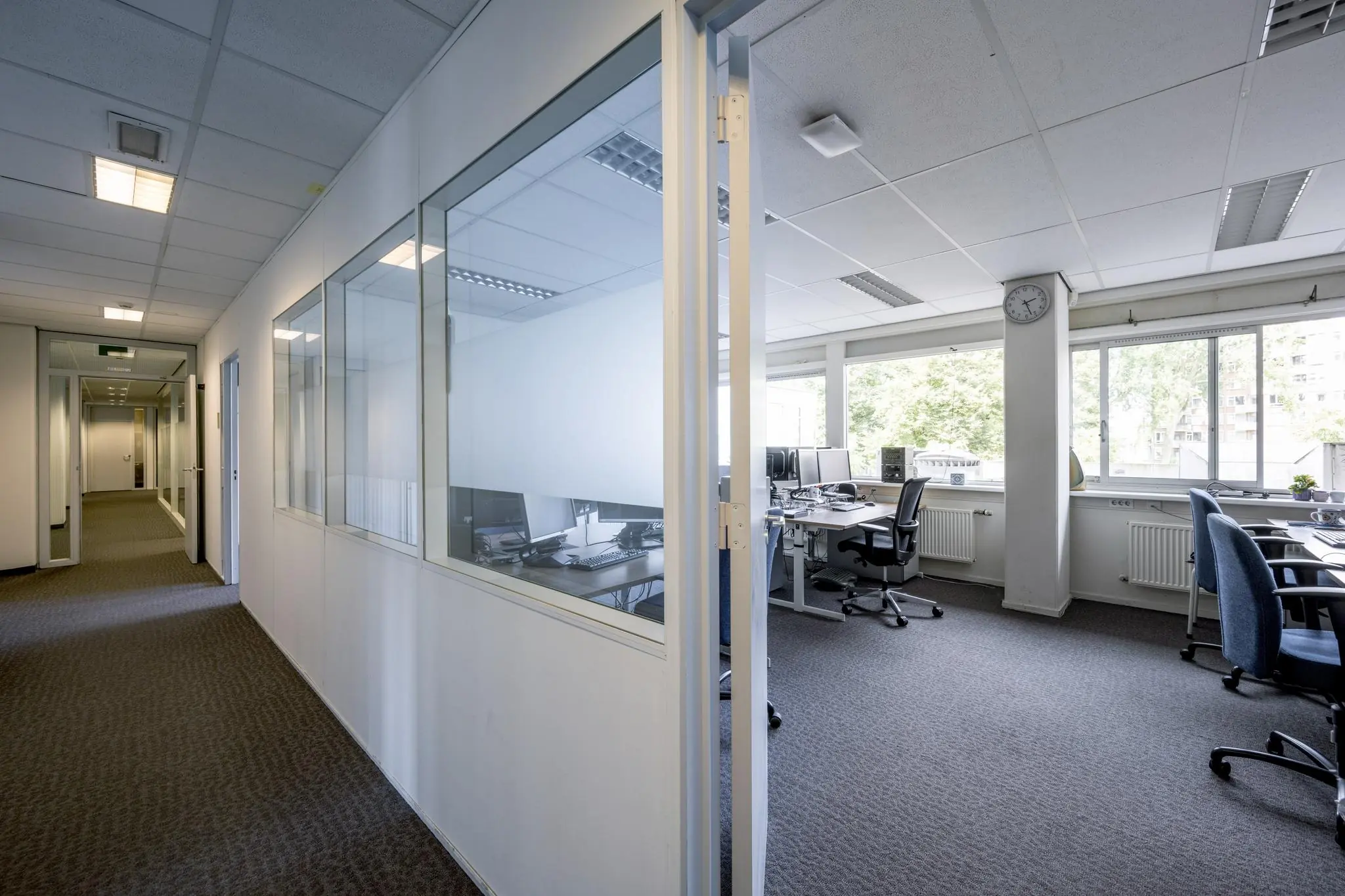 Modern kantoorinterieur aan de Jan Tooropstraat met werkplekken, grote ramen en een gang met glazen wanden.